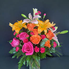 Mixed bouquet of orange and pink roses with lilies in a clear glass vase
