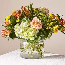 Mixed bouquet of peach roses, white hydrangea, and yellow flowers in a glass vase