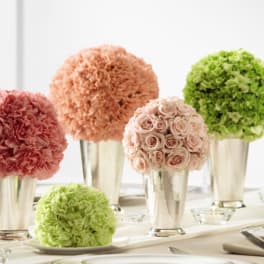 Cluster of pink, peach, and green round floral centerpieces in silver cups on an elegant table setting
