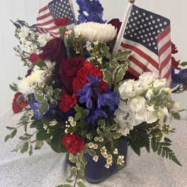 Red, white, and blue floral arrangement with two small American flags in a vase