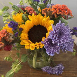 Mixed bouquet with a sunflower, purple chrysanthemums, and orange cockscomb in a glass vase