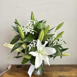 White lilies and baby's breath in a glass vase with a white ribbon