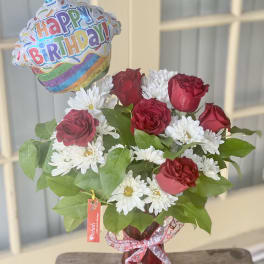 Red roses and white daisies in a vase with a birthday balloon
