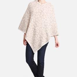Woman wearing a beige patterned poncho with dark jeans and black ankle boots