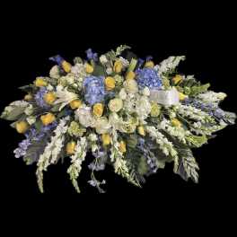 Large floral spray with yellow roses, white lilies, and blue hydrangeas