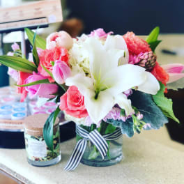Pink and white flower arrangement in a glass vase with a striped ribbon