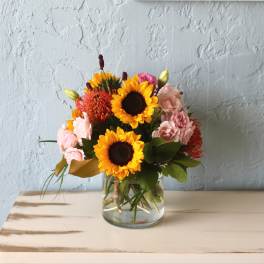 Sunflowers and pink flowers arranged in a clear glass vase