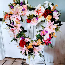 Heart-shaped floral wreath on a stand with pink, white, red, and orange flowers