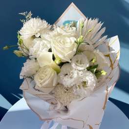 Bouquet of white and blush flowers wrapped in white paper with a ribbon