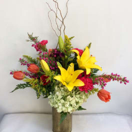 Colorful floral arrangement with yellow lilies and orange tulips in a tall vase