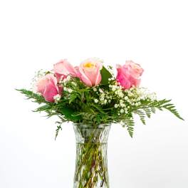Tall clear glass vase of pink roses with white filler flowers arranged in a loose bouquet