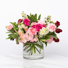 Pink roses, carnations, hydrangea, and white daisies in a clear glass vase