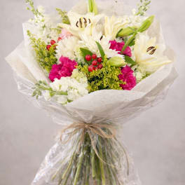 Bouquet of white lilies, pink carnations, and white chrysanthemums wrapped in paper