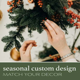Hands decorating a holiday wreath with pinecones and red berries