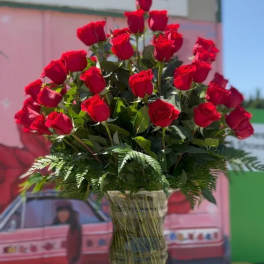 Tall vase arrangement of red roses with fern foliage