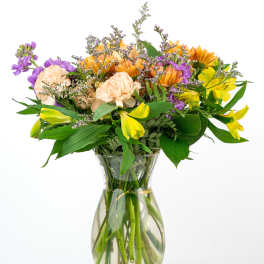 Mixed bouquet of yellow, purple, and peach flowers in a clear glass vase