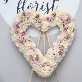 Heart-shaped floral wreath on an easel with pale pink and cream roses