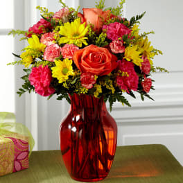 Bouquet of orange roses, yellow daisies, and pink carnations in a red vase