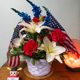 Basket arrangement with white lilies, red carnations, and blue flowers with American flags