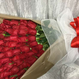 Large bouquet of tightly packed red roses wrapped in kraft paper with white mesh and a red bow.