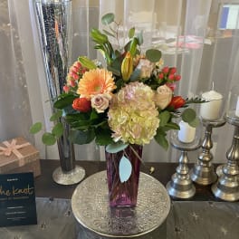 Mixed bouquet in a purple vase with candles and a gift box nearby