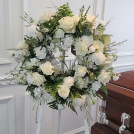 White rose and hydrangea funeral wreath on a stand beside a casket