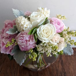 Pink and white bouquet of roses, peonies, and small white flowers in a glass vase