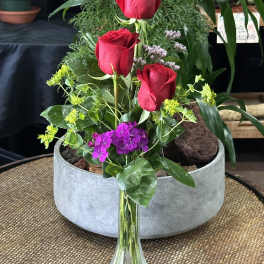 Three red roses in a clear glass vase with purple and yellow accents