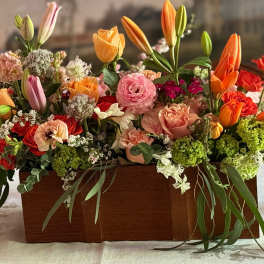 Rectangular wooden box filled with orange tulips, pink and peach roses, and mixed spring flowers