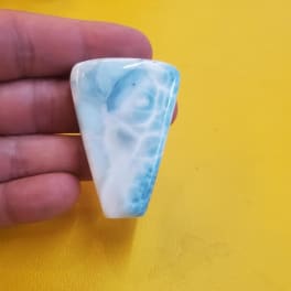 Hand holding a polished blue-and-white stone against a yellow background