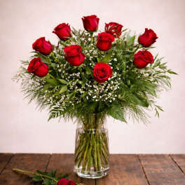 Red roses arranged in a clear glass vase with a single rose on the table
