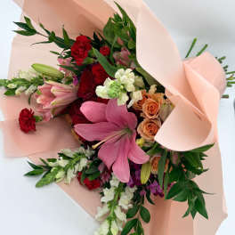 Bouquet of pink lilies, red carnations, and peach roses wrapped in blush paper