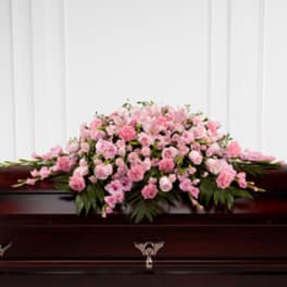 Pink floral casket spray on a dark wooden casket