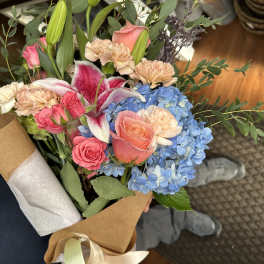 Hand-tied bouquet with pink roses, blue hydrangeas, lilies, and carnations