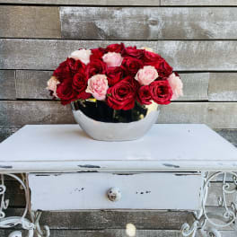 Red and blush roses arranged in a silver bowl on a white table