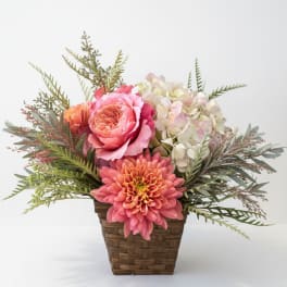Pink and peach flowers in a woven basket with airy greenery