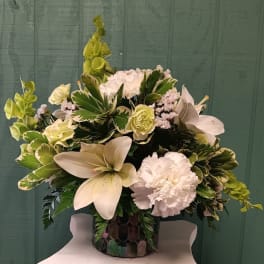 White lilies and carnations in a decorative vase with green foliage