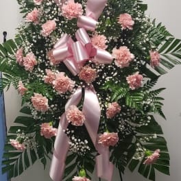 Pink carnation standing spray with a large pink ribbon on an easel