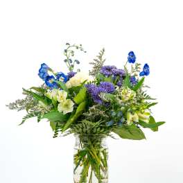 Mixed bouquet of blue, purple, and cream flowers in a clear glass jar vase