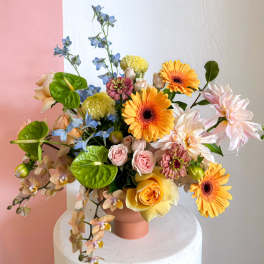 Mixed bouquet in a pink vase with orange, pink, blue, and white flowers