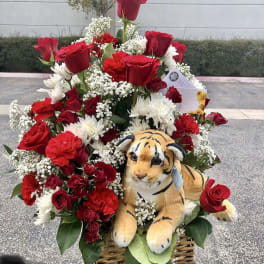 Basket arrangement of red roses, white daisies, and a plush tiger