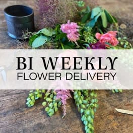 Loose floral arrangement with pink blooms and greenery beside a black cup