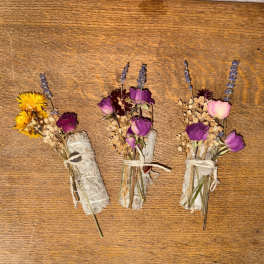 Three small dried flower and sage bundles tied with twine on a wooden surface