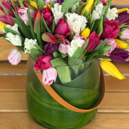 Mixed tulip bouquet in a green glass vase with a tan handle