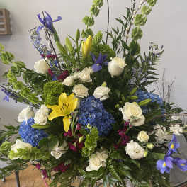 Large mixed floral arrangement with blue hydrangeas, white roses, and yellow lilies