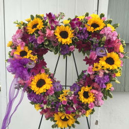 Heart-shaped floral wreath with sunflowers, purple and pink blooms, and a ribbon