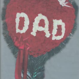 Heart-shaped red floral tribute with white letters and ribbon
