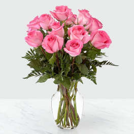 Dozen pink roses arranged in a clear glass vase on a light surface