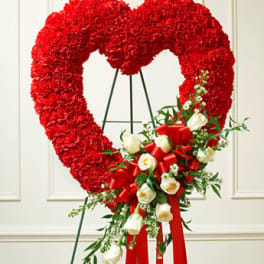 Heart-shaped red floral wreath on an easel with white roses and a red ribbon spray