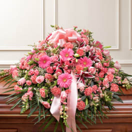 Large pink floral casket spray with ribbon on a wooden casket